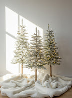 Windsor Flock artificial Christmas trees, pre-lit with warm white twinkle LED lights, in three sizes on a white fur rug