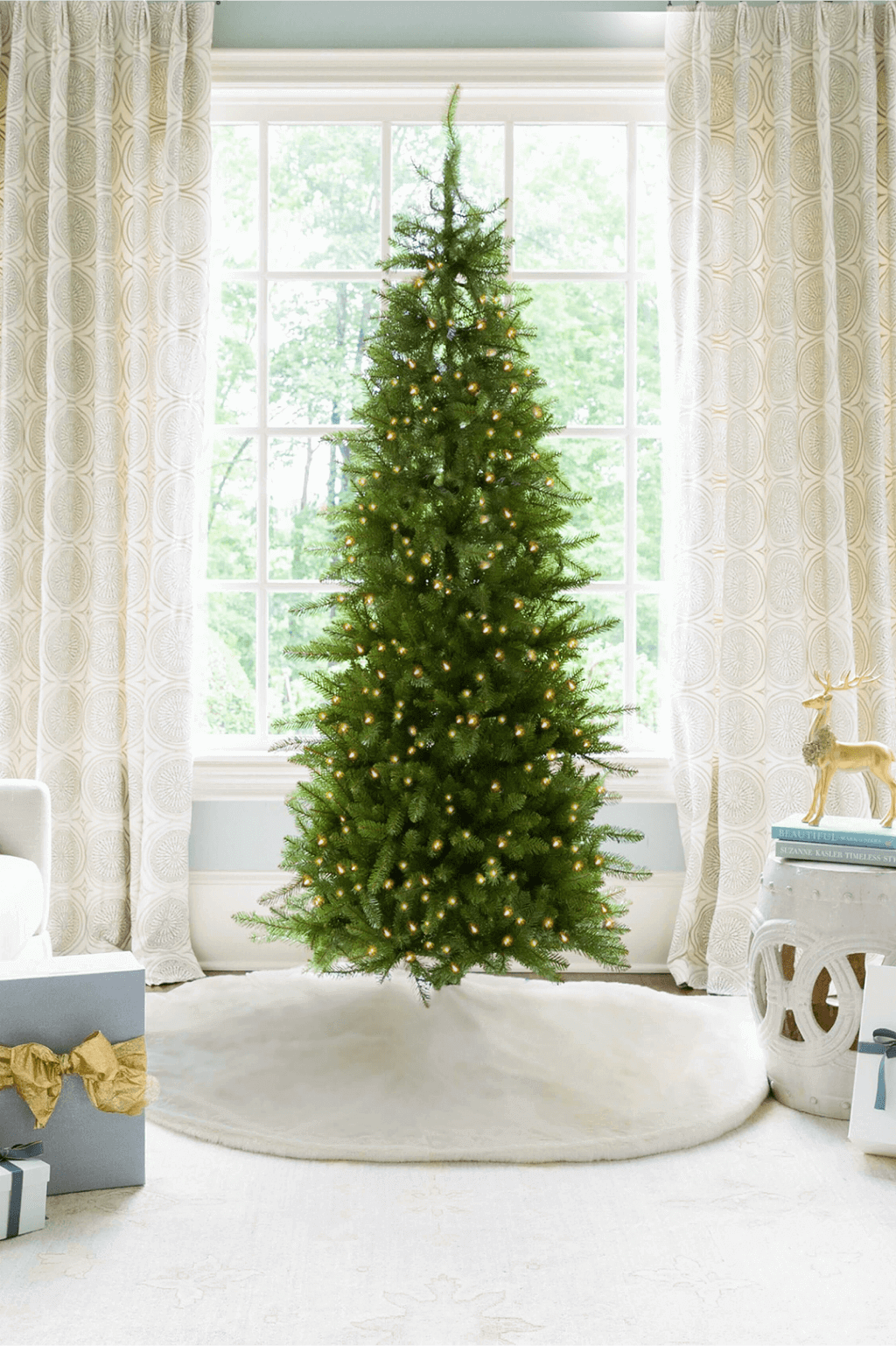 6.5 ft Yorkshire Fir Slim artificial Christmas tree, glowing with warm white LED lights in front of a large window