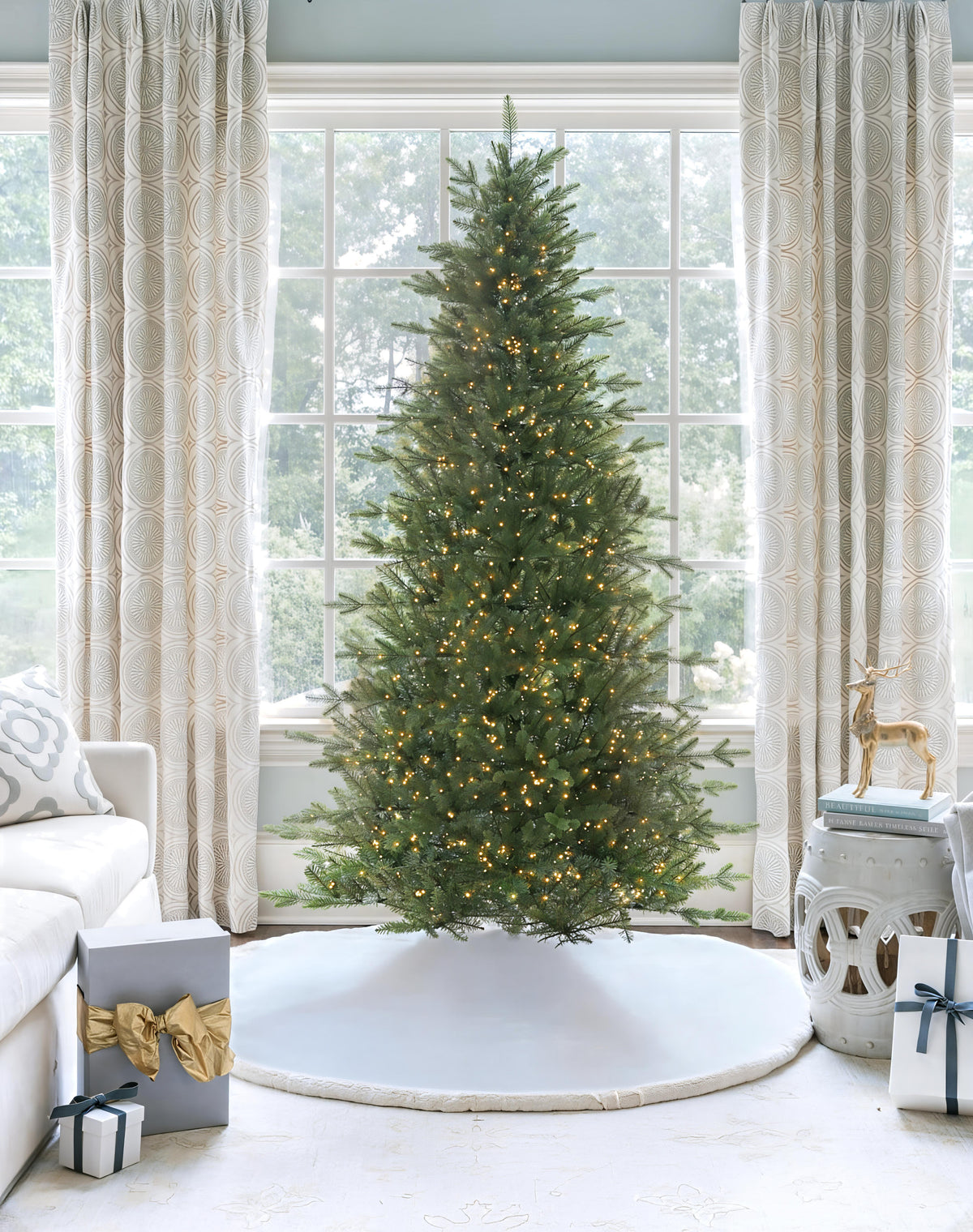 Alpine Fir Slim artificial Christmas tree, pre-lit with Lux LED lights, standing in front of a large window with a white tree skirt