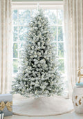7.5 ft King Flock artificial Christmas tree, glowing with warm white lights in front of a large window