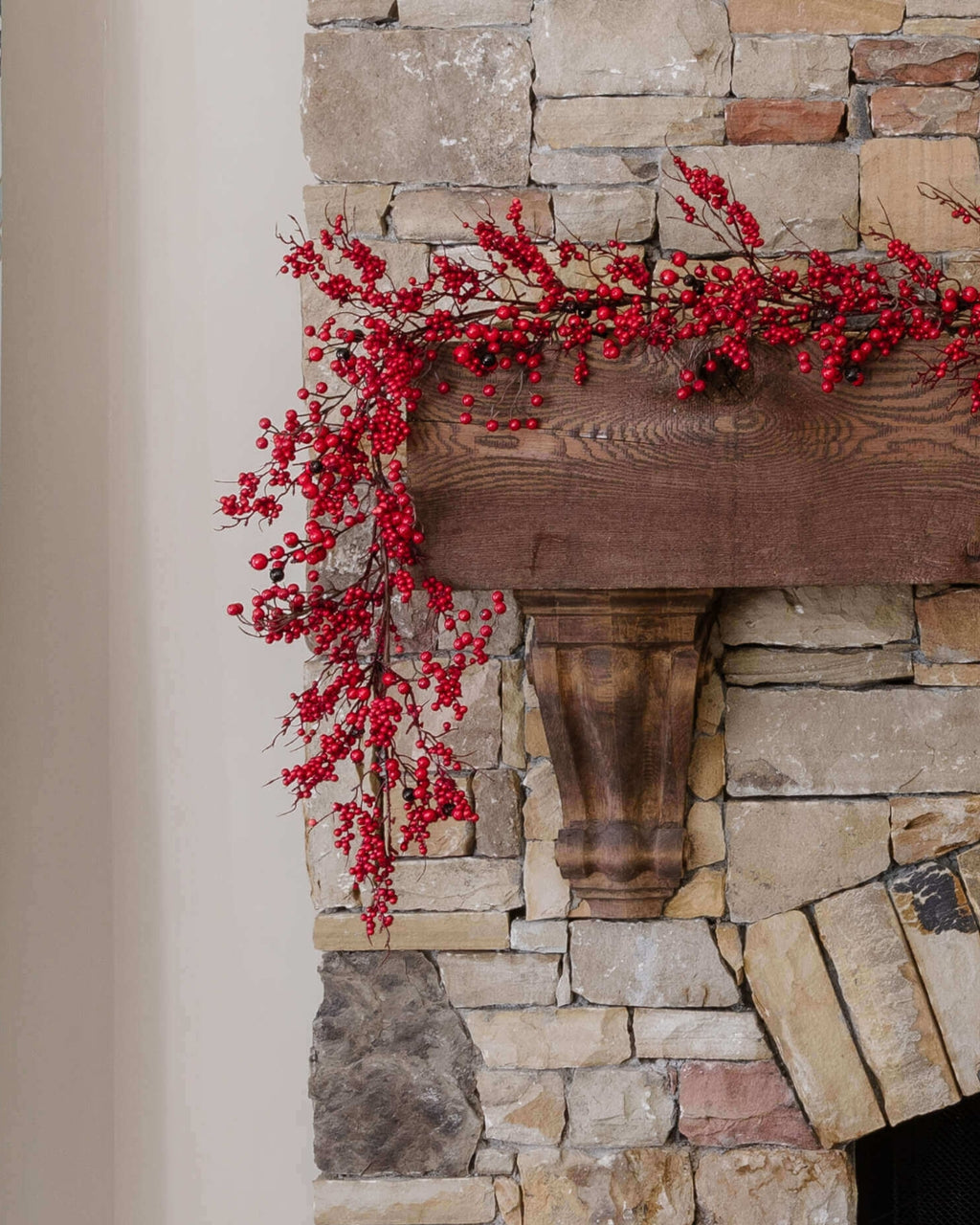 9 ft Berry artificial Christmas garland, unlit, with red berries draped over a stone fireplace mantel