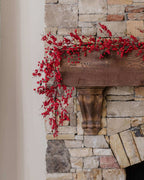 9 ft Berry artificial Christmas garland, unlit, with red berries draped over a stone fireplace mantel