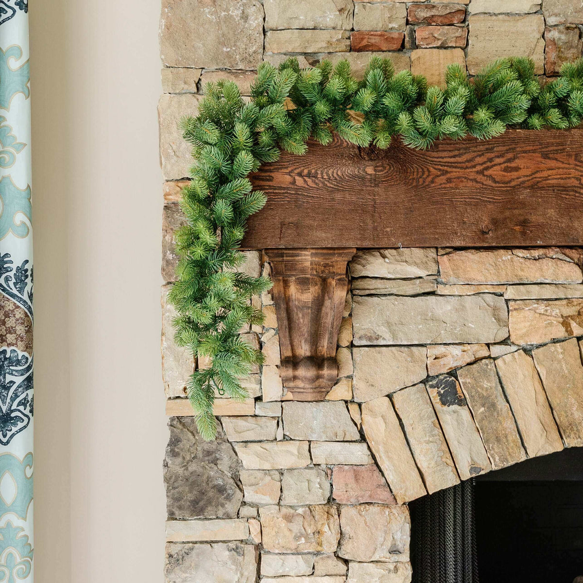 9 ft Royal Fir artificial Christmas garland, pre-lit with warm white LED lights, draped over a stone fireplace mantel