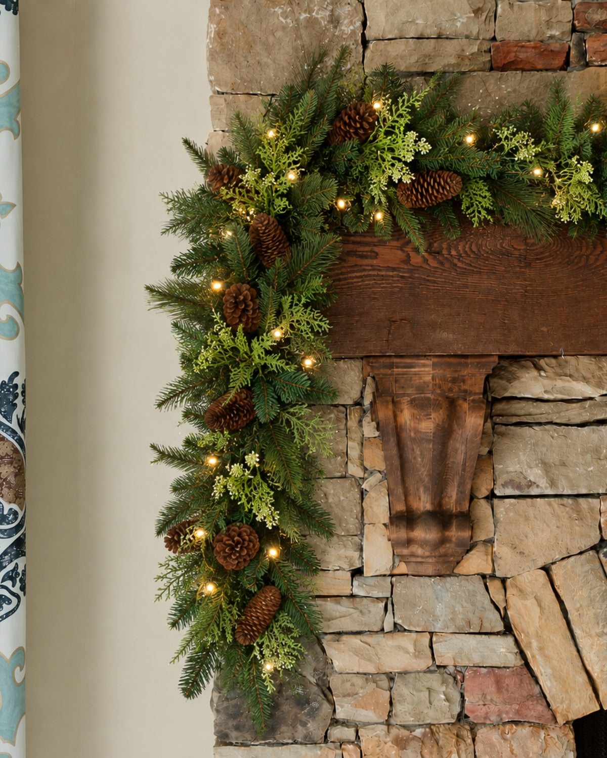 9 ft Woodland Lodge artificial Christmas garland with pinecones, glowing with warm white LED lights on a stone fireplace mantel