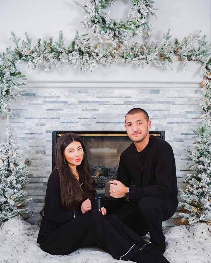 Couple seated by a white fireplace with flocked garland, King of Christmas customer photo by @gigigumrika