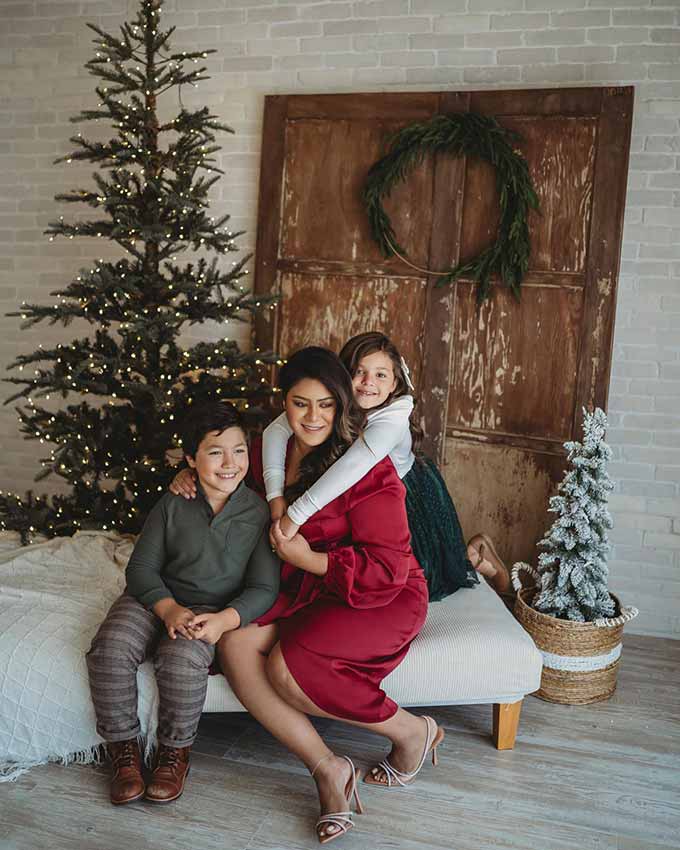 Family on a bench in front of slim green trees and a wreathed wood door, King of Christmas customer photo by @georgescuphotography
