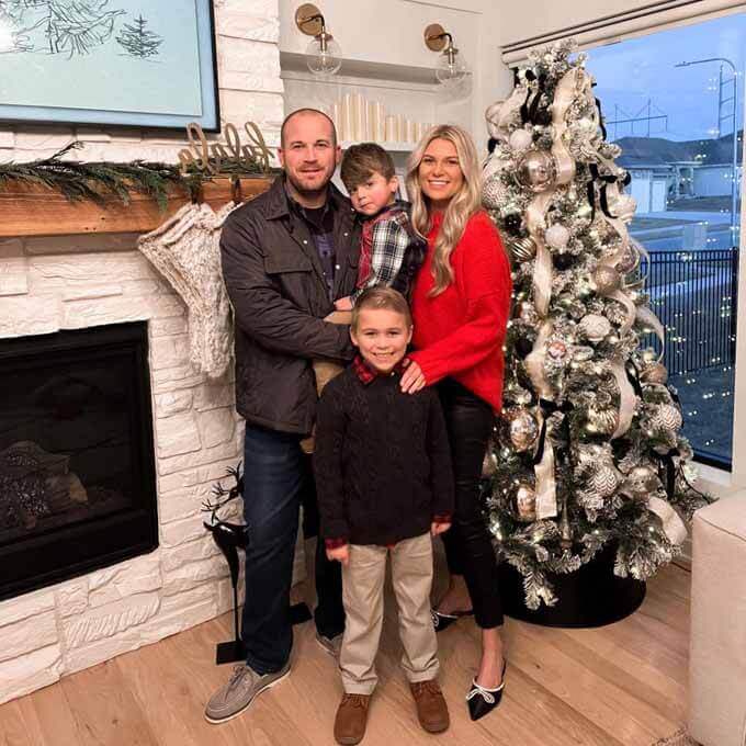 Family of four by a flocked tree and fireplace, King of Christmas customer photo by @notednatalie