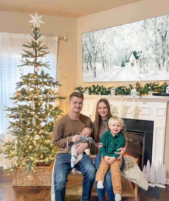 Family on a sofa beside a lit tree and fireplace, King of Christmas customer photo by @alli_mateush