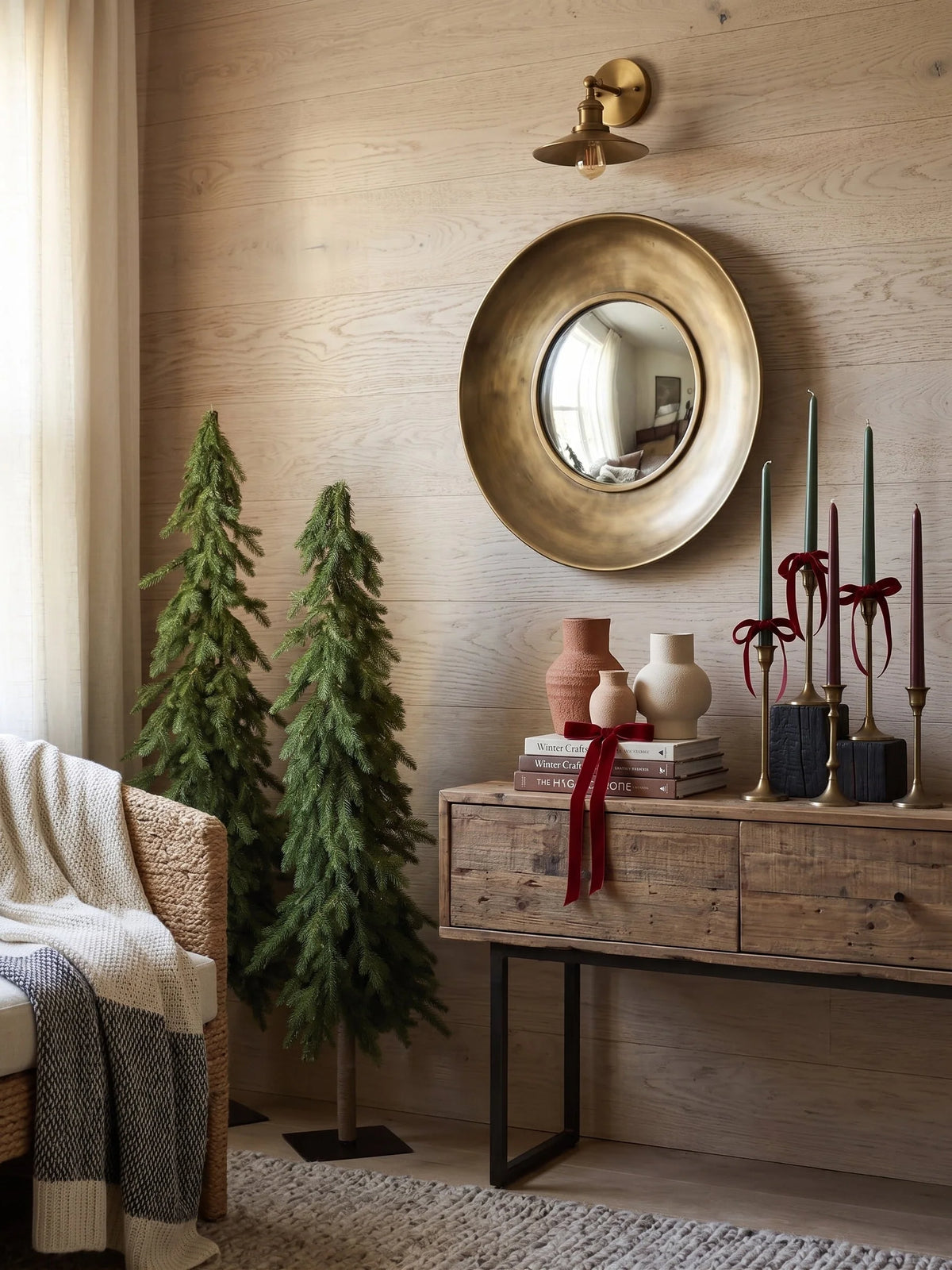 Two slim accent artificial Christmas trees flanking an entryway console beneath a round mirror