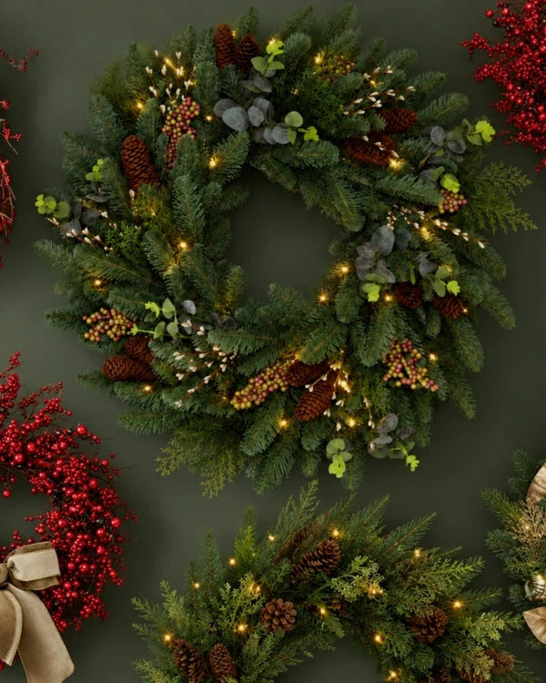 Artificial Christmas wreath and red berry garland on a dark green wall