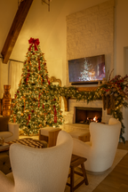 King Fraser Fir artificial Christmas tree, glowing in a cozy living room beside the fireplace