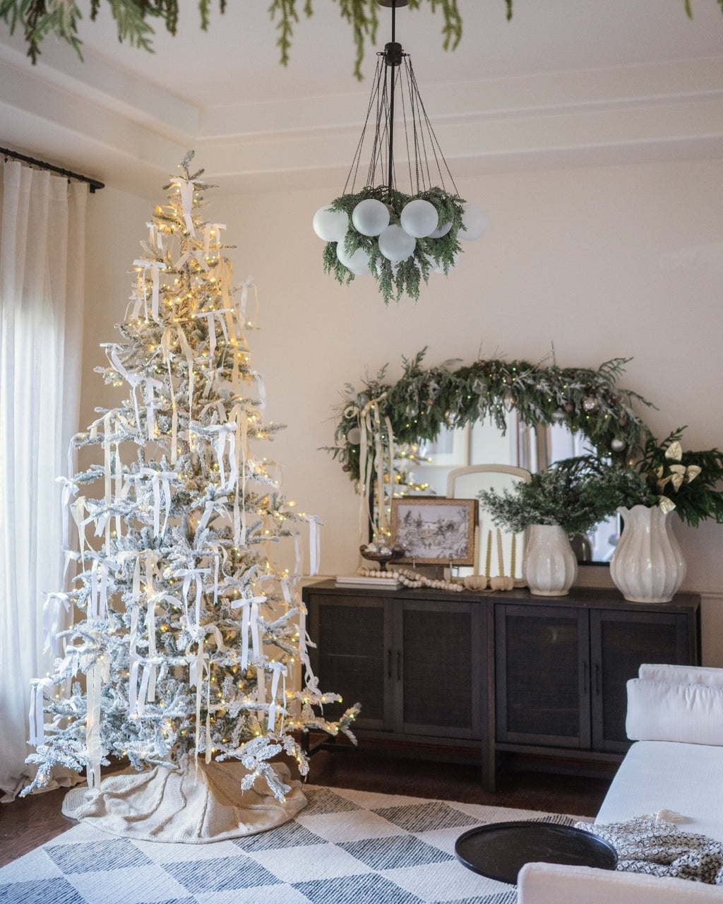 King Noble Flock artificial Christmas tree, decorated and glowing in a living room with a chandelier and wreath