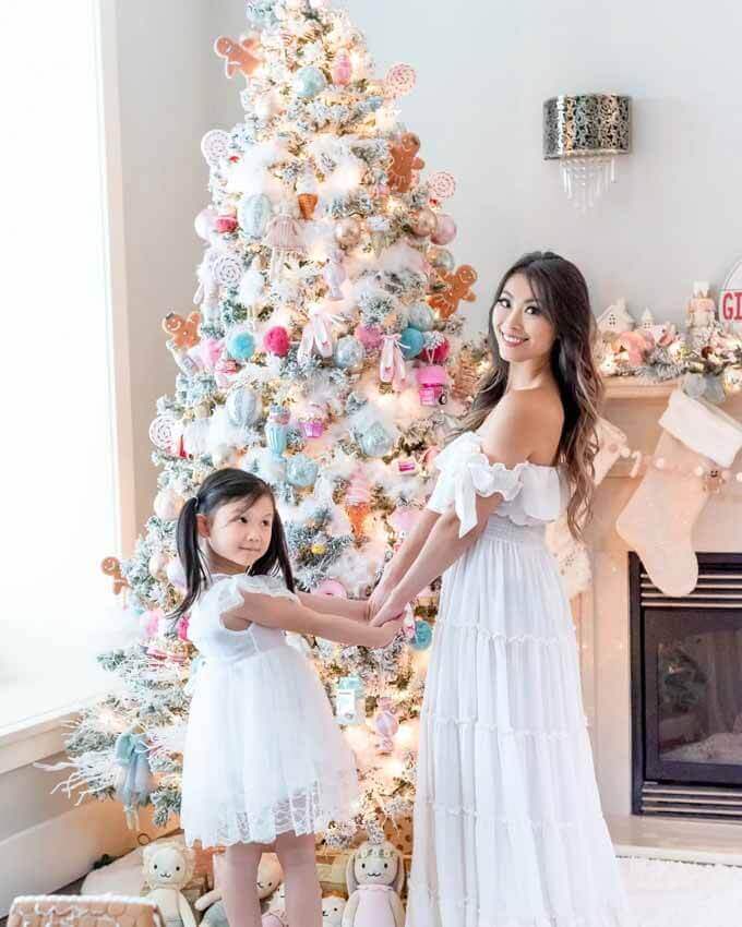 Mother and daughter in white dresses by a pink-decorated flocked tree, King of Christmas customer photo by @dmak.xo