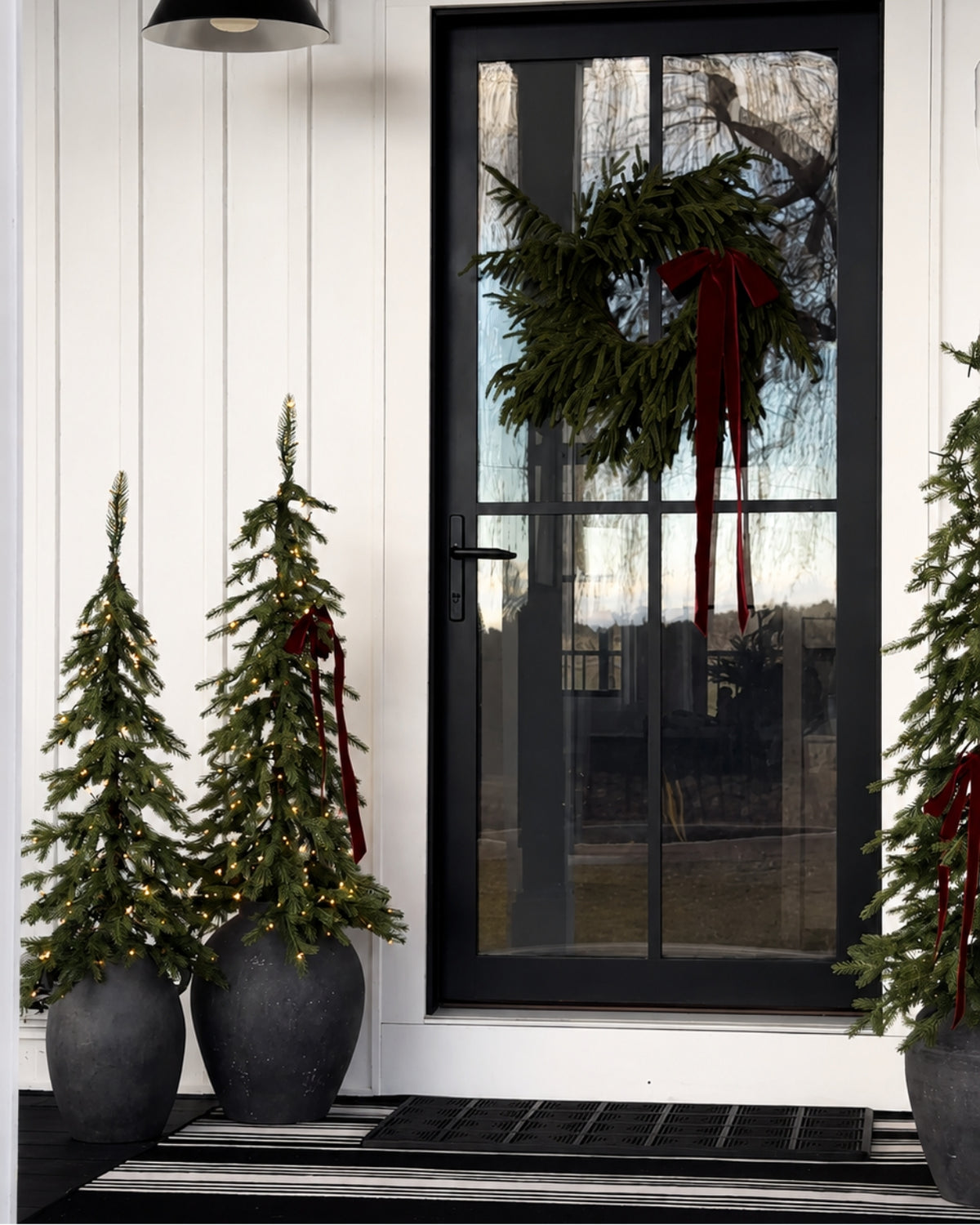 Pair of Windsor Fir artificial Christmas trees, pre-lit with warm white twinkle LED lights, flanking a black front door