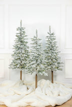 Three Windsor Flock artificial Christmas trees, pre-lit with warm white twinkle LED lights, against a white paneled wall