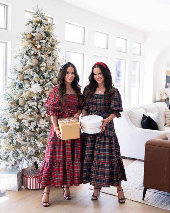 Two women in plaid dresses beside a flocked tree, King of Christmas customer photo by @thedoubletakegirls