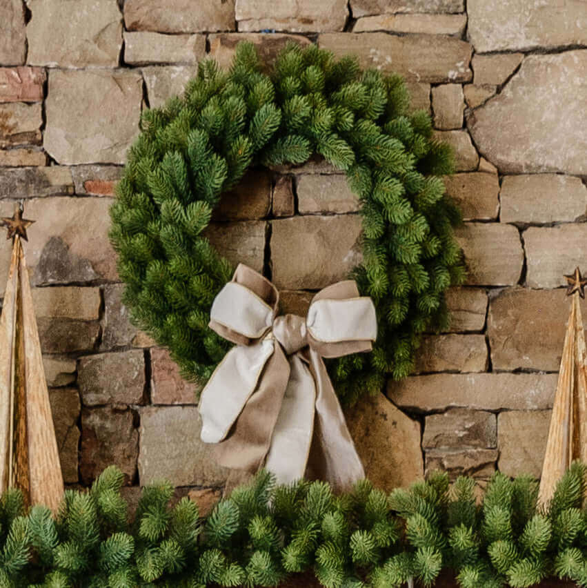 24 in Royal Fir artificial Christmas wreath, unlit, with a cream ribbon bow on a stone wall