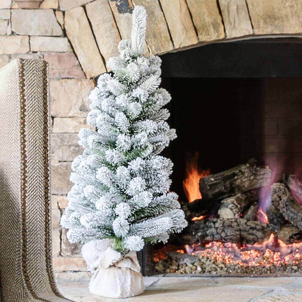 3 ft King Flock artificial Christmas tabletop tree with a burlap-wrapped base beside a stone fireplace