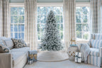 6 ft Prince Flock artificial Christmas tree, pre-lit with warm white LED lights, in front of large windows between two armchairs