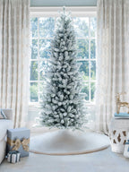 7.5 ft King Flock Slim artificial Christmas tree, standing in front of a large window with a white tree skirt