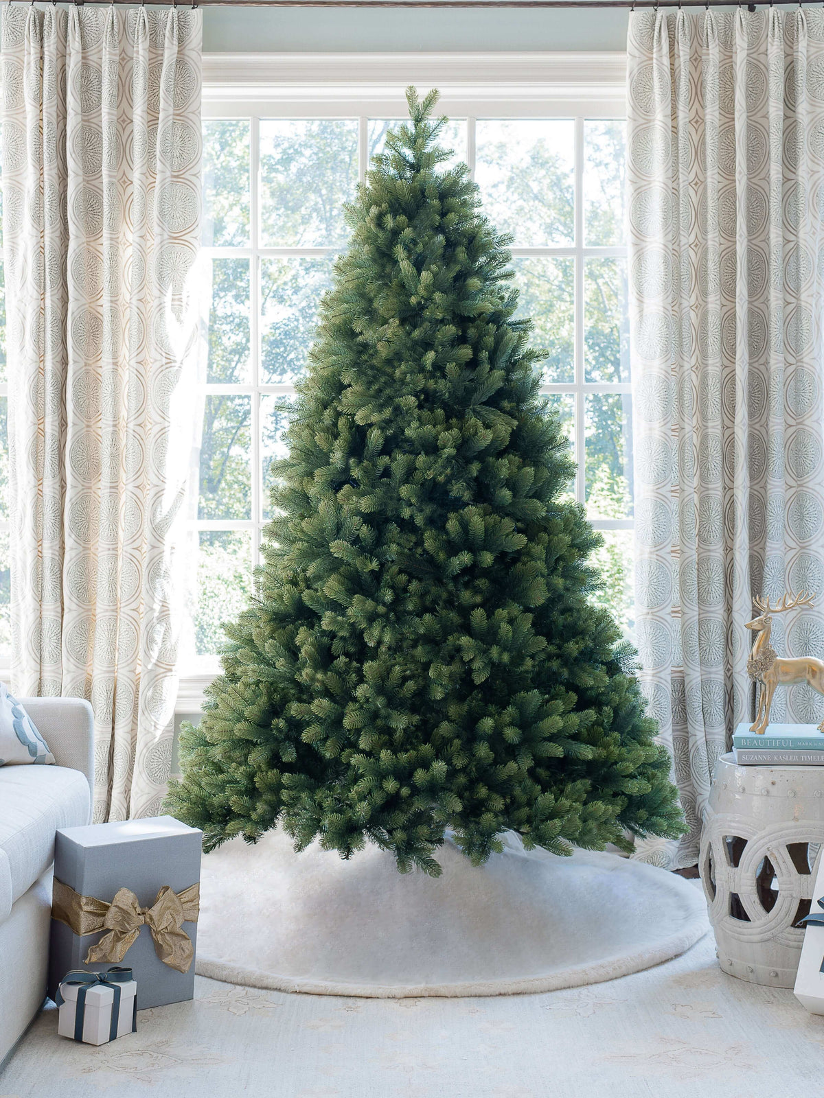 7.5 ft Royal Fir artificial Christmas tree, pre-lit with warm white and multicolor LED lights, standing in front of a large window with a white tree skirt