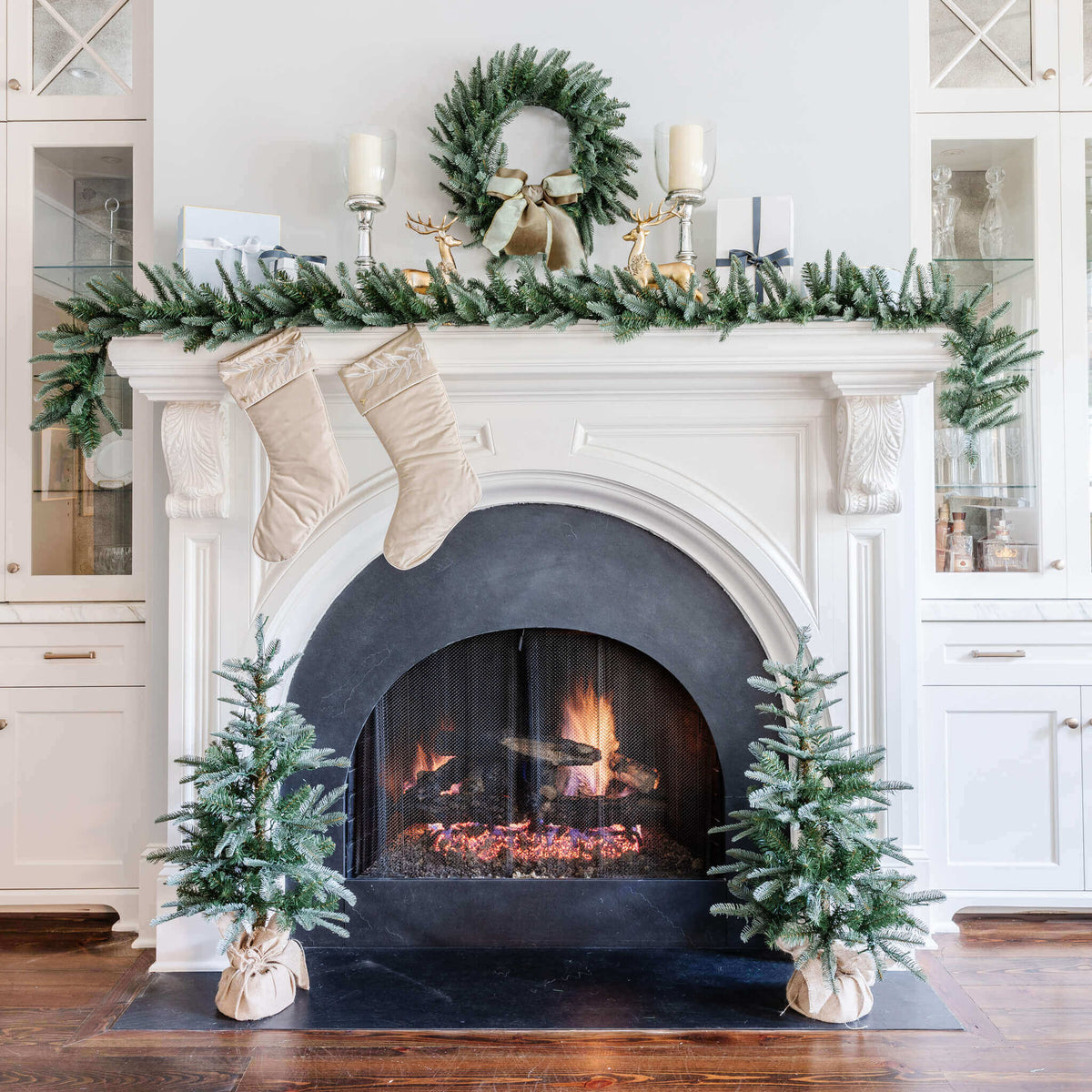King Noble Fir tree, wreath, garland and tabletop trees around a white fireplace with stockings