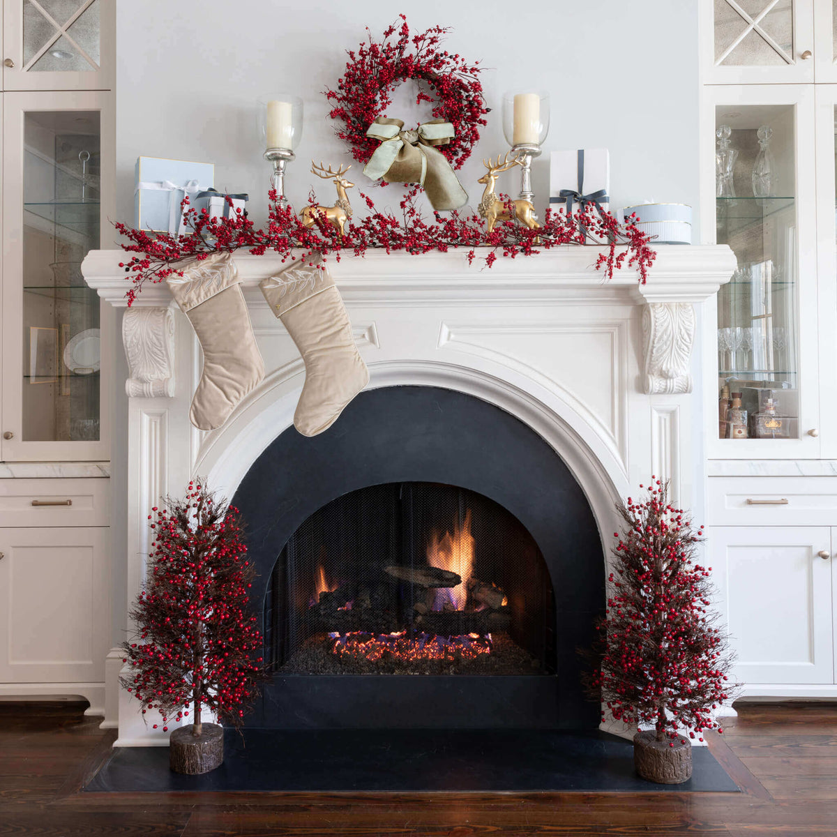 Red Berry wreath, garland and tabletop trees on a white fireplace with stockings